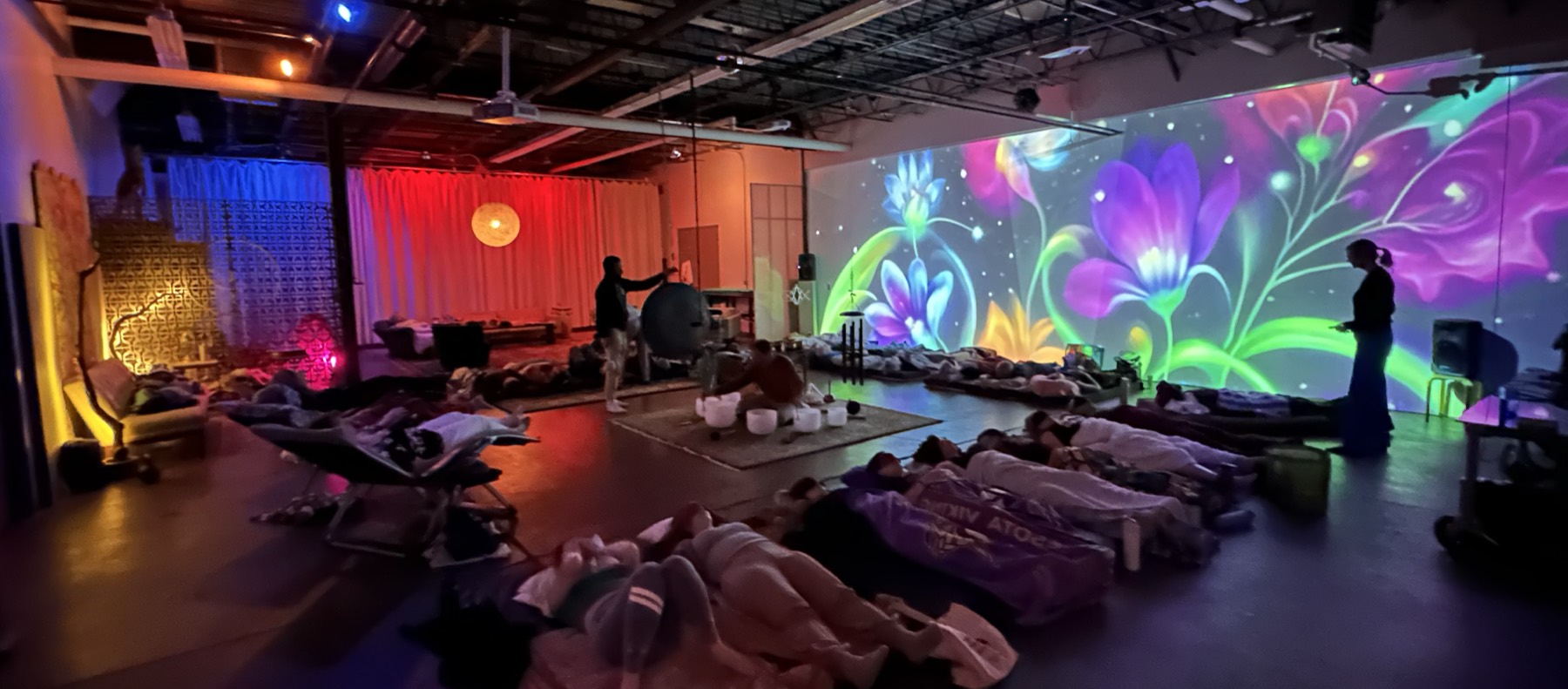 A sound bath in progress — guests resting on the floor as flower light projection fills the wall