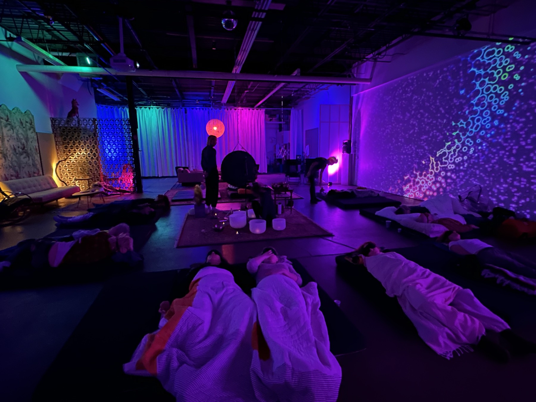 The gong and practitioners as guests rest under blankets in low purple light